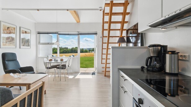 A modern kitchen with a built-in stove, a coffee maker, and a view of a green landscape through the open door. - Lovely apartment in Allinge (Allinge)