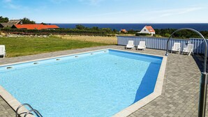 A rectangular swimming pool with a clear blue water surface, surrounded by a paved deck with white lounge chairs. - Lovely apartment in Allinge (Allinge)