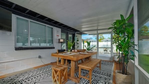 Uma área de refeições com mesa e bancos de madeira, rodeada por tapetes estampados e plantas em vasos.