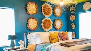Quarto com cama, mesa de cabeceira, luminária e arte decorativa na parede.