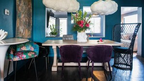 Uma sala de jantar moderna com uma mesa de madeira, cadeiras roxas e um vaso branco com flores.