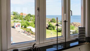 A room with large windows offering a view of a coastal area with greenery and a beach. - 2 bedroom lovely apartment in Gudhjem (Gudhjem)
