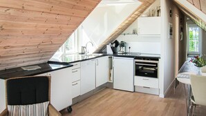 A modern kitchen with a sloped ceiling, white cabinetry, a black countertop, and a built-in oven. - 2 bedroom lovely apartment in Gudhjem (Gudhjem)