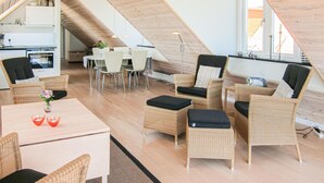 A modern loft apartment with a sloped ceiling, a dining area with white chairs, wicker furniture, and a kitchen with white cabinets. - 2 bedroom lovely apartment in Gudhjem (Gudhjem)