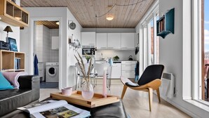 Een moderne woonkamer met een bank, een salontafel met tijdschriften, een eethoek met een stoel en een keuken op de achtergrond.