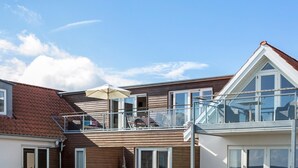 Een modern herenhuis met balkon, grote ramen en een pannendak.