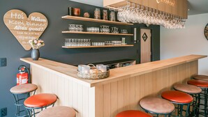 Un espace bar avec un comptoir en bois, de nombreux tabourets, des étagères remplies de verres et un panneau lumineux au néon.