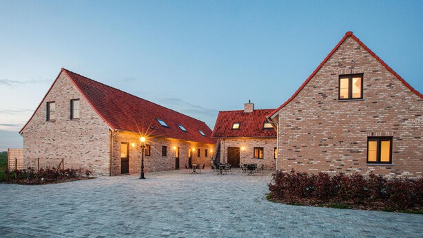 Un bâtiment en briques avec un toit recouvert de tuiles rouges, de nombreuses fenêtres et des places assises à l’extérieur.