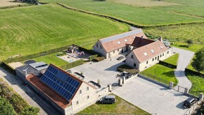 Une grande ferme dotée d’une allée spacieuse, d’une installation de panneaux solaires et d’un espace de jeux pour enfants.