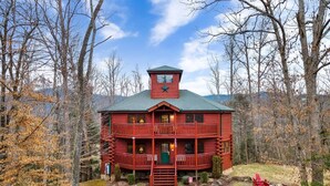 A red log cabin with a balcony and a small tower, surrounded by trees and a gravel path. - Smoky Mountain Fall Colors Private Pool Hot Tub Theater and Cozy Mountain Escape (Cosby)