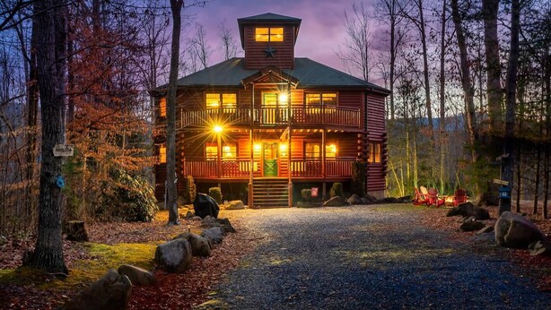 A two-story log cabin with a balcony, surrounded by trees and a gravel driveway. - Smoky Mountain Fall Colors Private Pool Hot Tub Theater and Cozy Mountain Escape (Cosby)