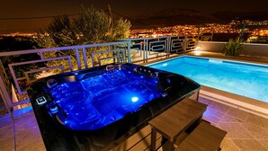 Ett bubbelbad med en kontrollpanel, omgivet av en pool och ett räcke, med utsikt över staden i bakgrunden.
