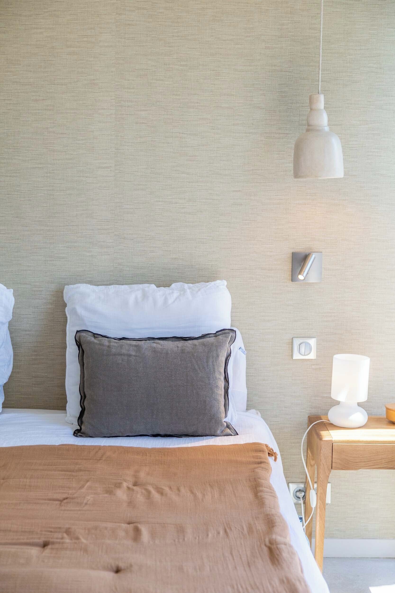 Una cama bien hecha con almohadas, una mesita de noche con lámpara y una lámpara colgante.