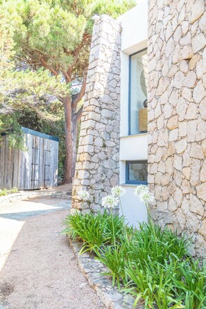 A stone building with a modern design, a wooden fence, and a pathway with green plants.