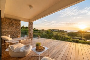 A wooden deck with outdoor furniture, a stone wall, and a view of the landscape.