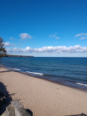 Une plage avec une promenade en bois menant à l’eau, un ciel dégagé et une terre lointaine à l’horizon.