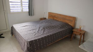 Un dormitorio con cama, mesita de noche, lámpara, ventana con cortinas y puerta.