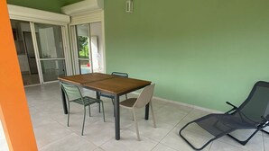 Un patio techado con una mesa y sillas, una silla reclinable y una puerta corrediza de vidrio que da a una cocina.
