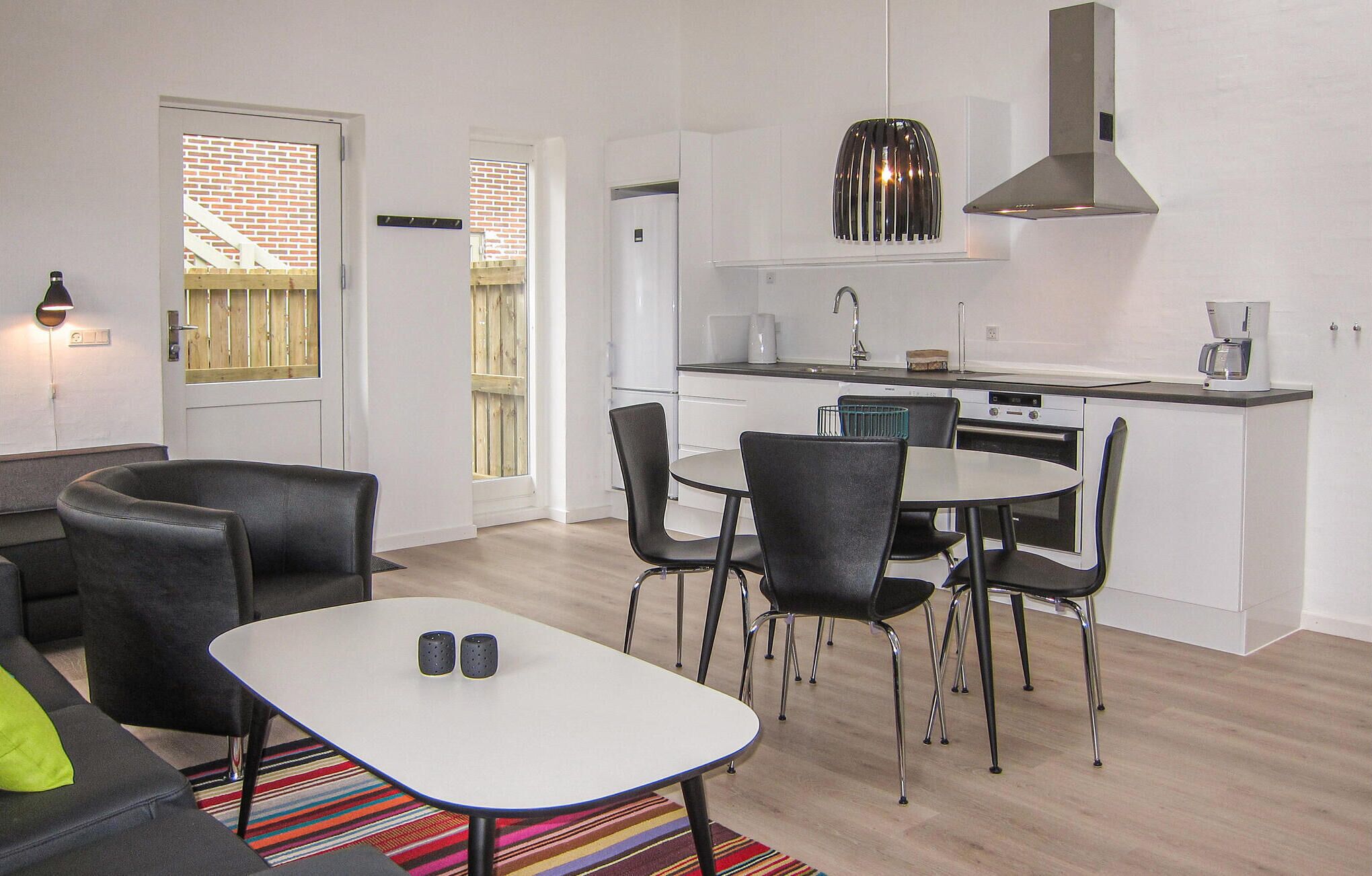 Un espacio habitable compacto con kitchenette, una zona de comedor con cuatro sillas, una mesita y un sofá.