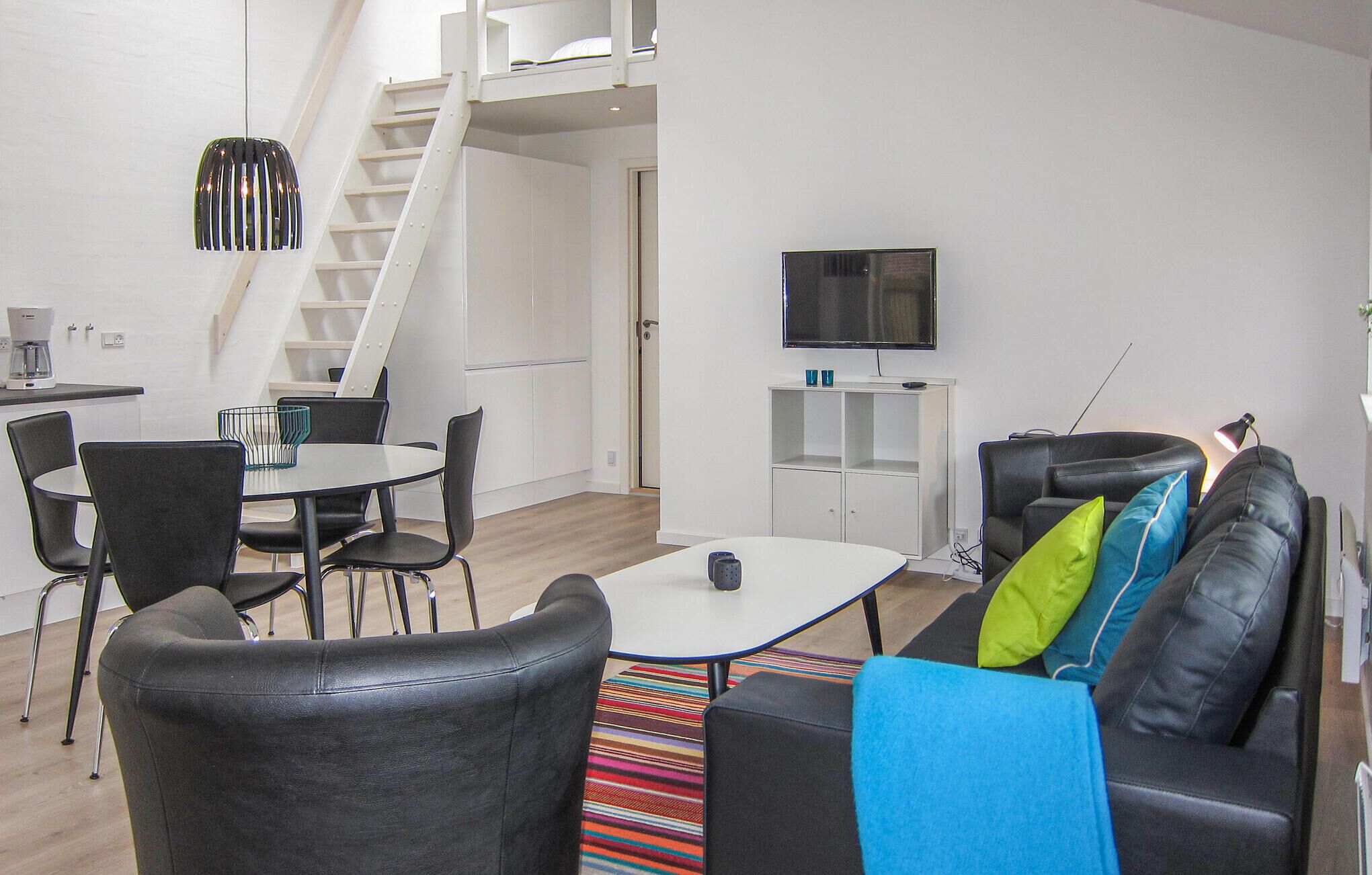 Un espacio moderno para vivir con una escalera, un área de comedor, un sofá con cojines de colores y un televisor.