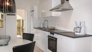 Una cocina moderna con armarios blancos, campana extractora de acero inoxidable, horno integrado, cafetera y un comedor con mesa y sillas.