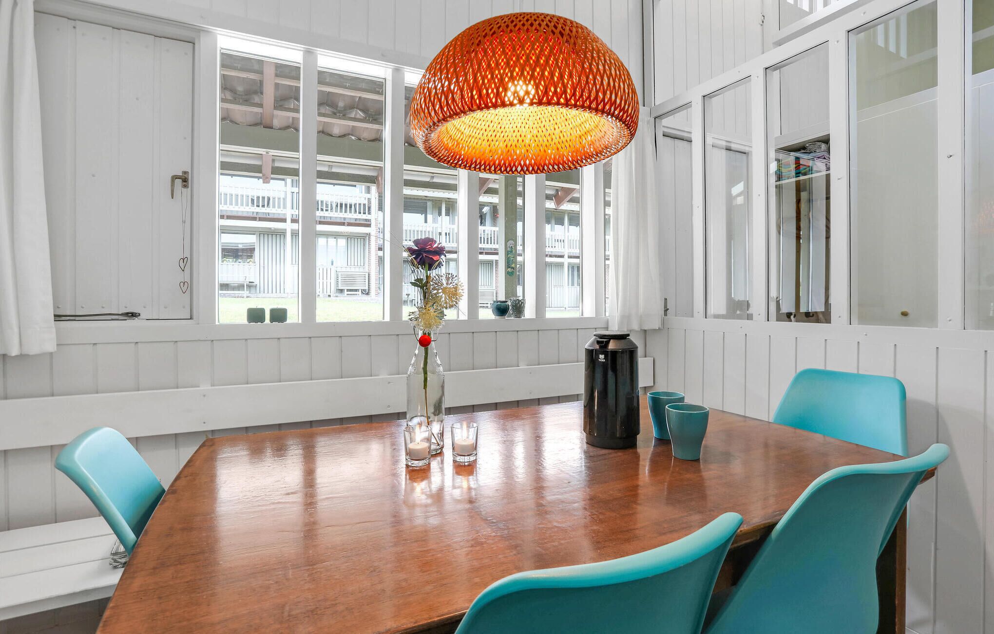 Ein Konferenzraum mit einem Holztisch, blaugrünen Stühlen, einer großen orangefarbenen Pendelleuchte und einer Vase mit Blumen.