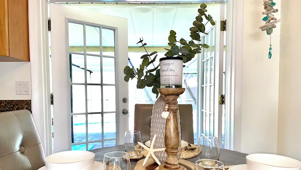 Mesa de comedor dispuesta con platos blancos, cubiertos y cristalería, con un centro de mesa decorativo y una planta en maceta.