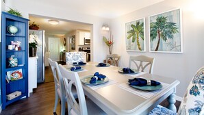 Een eethoek met een witte tafel voor vier personen, blauwe servetten en een blauwe kast met decoratieve objecten.