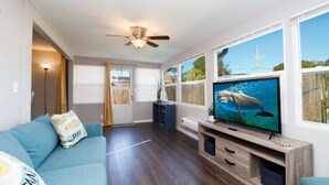 Een woonkamer met een televisie, een plafondventilator, een blauwe bank en een houten tv-meubel.