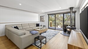 Una sala de estar moderna con un sofá modular, una mesa de centro, una chimenea y ventanas amplias con vistas al exterior.