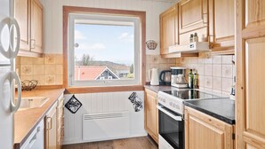 Ett kök med träskåp, ett fönster med utsikt över hus, en spis och en kaffebryggare.