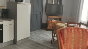 A compact living space with a kitchenette, a flat-screen TV, a wooden chair, and a patterned sofa.