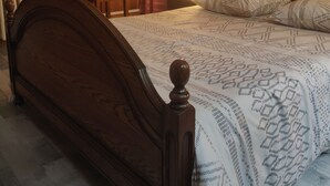 A wooden bed with a headboard, a bedside table with a lamp, and a window with curtains.