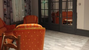 A room with a wooden floor, a sofa, a chair, and a table. There is a door with glass panels and a window with curtains.