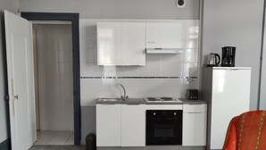 A compact kitchen with white cabinets, a sink, and a black dishwasher. There's a small round table and a red upholstered chair.