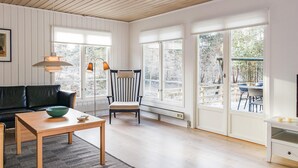 Een ruime woonkamer met een zwarte leren bank, een houten tafel met een groene kom, en een gestreepte stoel. Grote ramen bieden uitzicht op een besneeuwd terras.