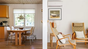Een eetgedeelte met een houten tafel en stoelen, een raam met jaloezieën en een airconditioner aan de muur.