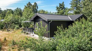 Een klein houten blokhut met een donker dak, omringd door weelderige begroeiing en bomen.