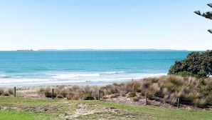 Un paysage côtier offrant une vue dégagée sur l’océan, avec un navire à l’horizon et une zone herbeuse délimitée par une clôture.