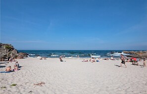 Een zandstrand met mensen die zonnebaden en zwemmen, rotskliffen aan de ene kant, en rustige golven in de oceaan.