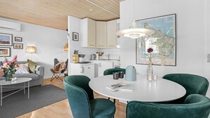Una sala de estar moderna con una mesa redonda blanca, sillas de terciopelo verde, un sofá gris y un techo de madera.