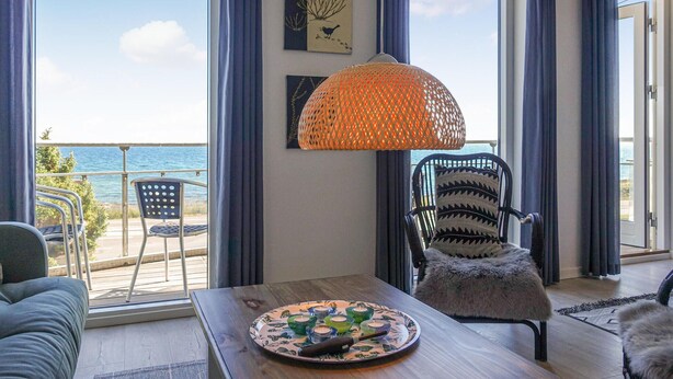 Een kamer met uitzicht op zee, een rieten lamp, een stoel en een tafel met kaarsen.
