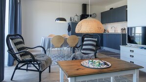 Een moderne woonkamer met een eethoek, met rieten stoelen, een houten salontafel en een grote geweven lamp.
