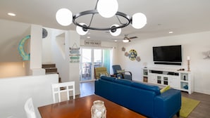 A modern living room with a blue sofa, a wooden dining table, and a chandelier. - 326 San Luis (Pismo Beach)