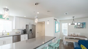 A modern kitchen with white cabinets, stainless steel appliances, and a central island with bar stools. - 326 San Luis (Pismo Beach)