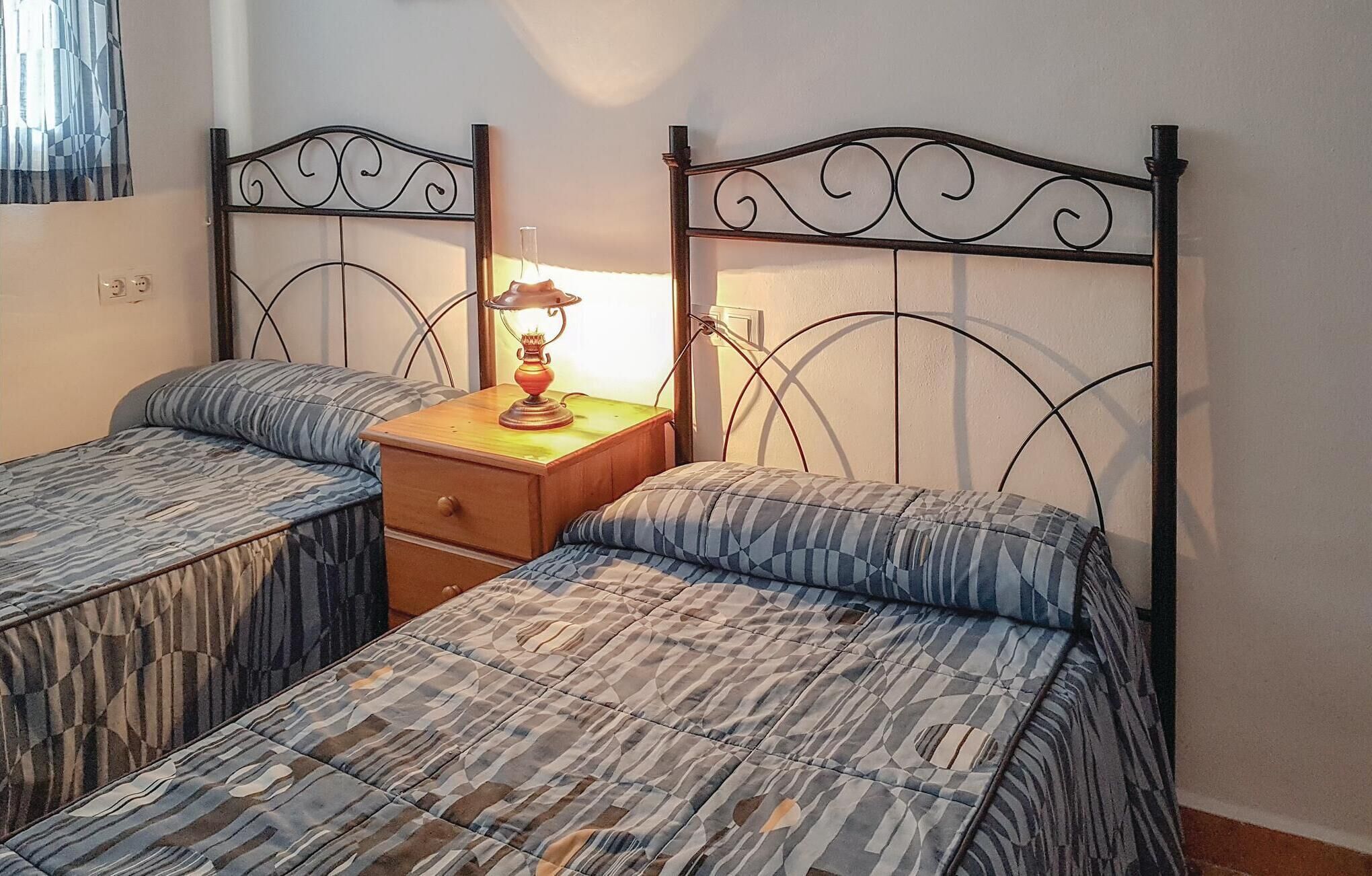 A room with two single beds, a wooden nightstand with a lamp, and a window with curtains.