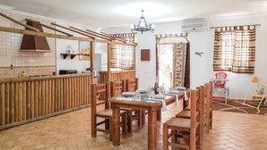 A dining area with a wooden table set for four, surrounded by wooden chairs. A chandelier hangs from the ceiling, and there are two windows with patterned curtains. - Cozy home in El Coronil (El Coronil)