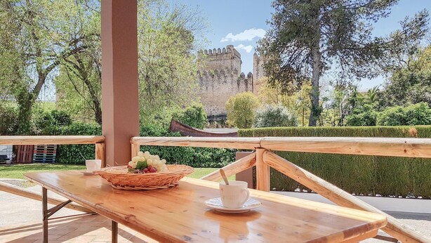 A wooden table with a basket of fruit and a cup, set against a backdrop of a castle and lush greenery. - Cozy home in El Coronil (El Coronil)