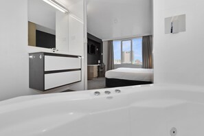 A modern hotel room with a large white bathtub, a bed, and a desk with a chair. - Allurity Hotel (Hobart)