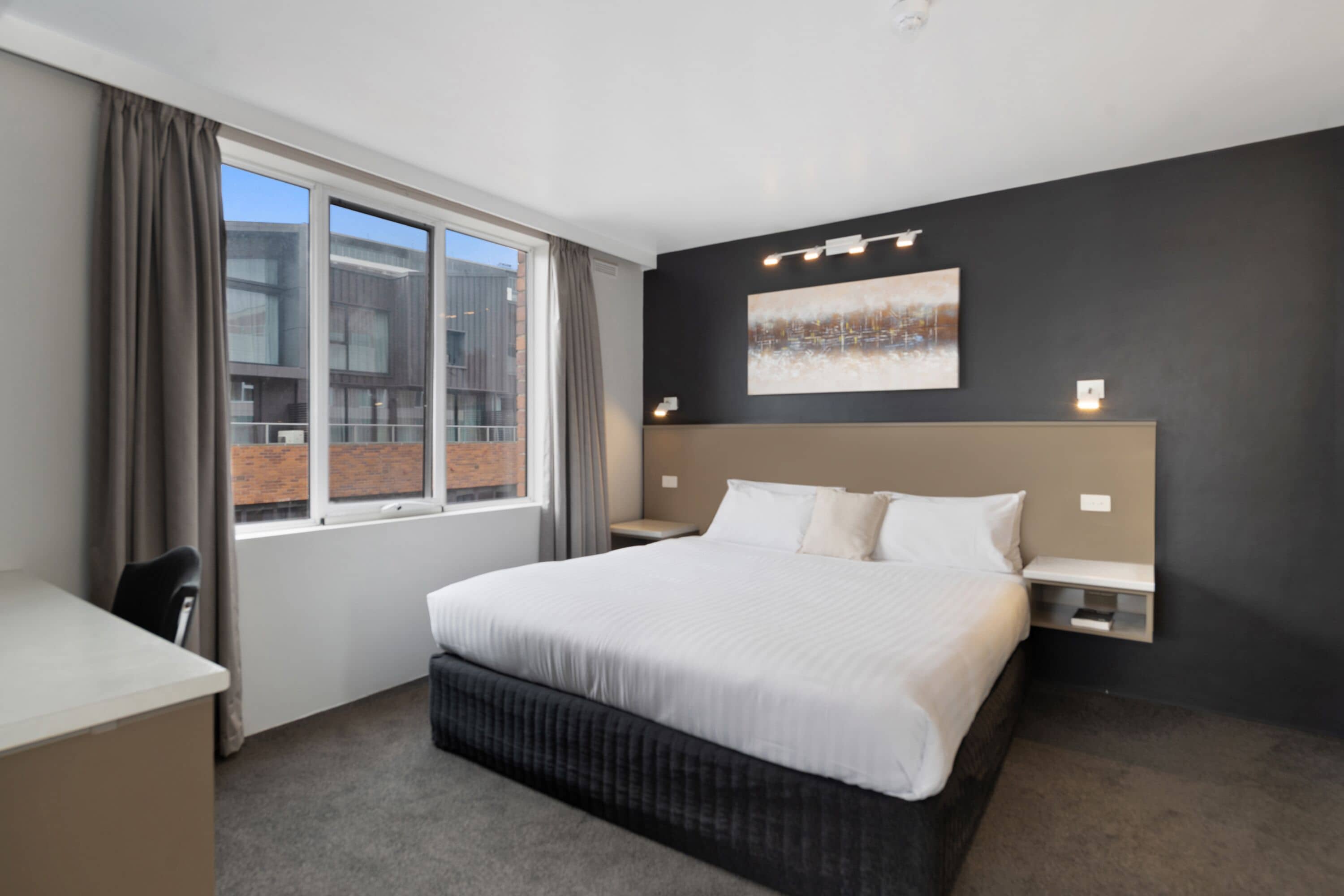 Una habitación de hotel moderna con una cama grande, un escritorio, una silla y una ventana con cortinas.